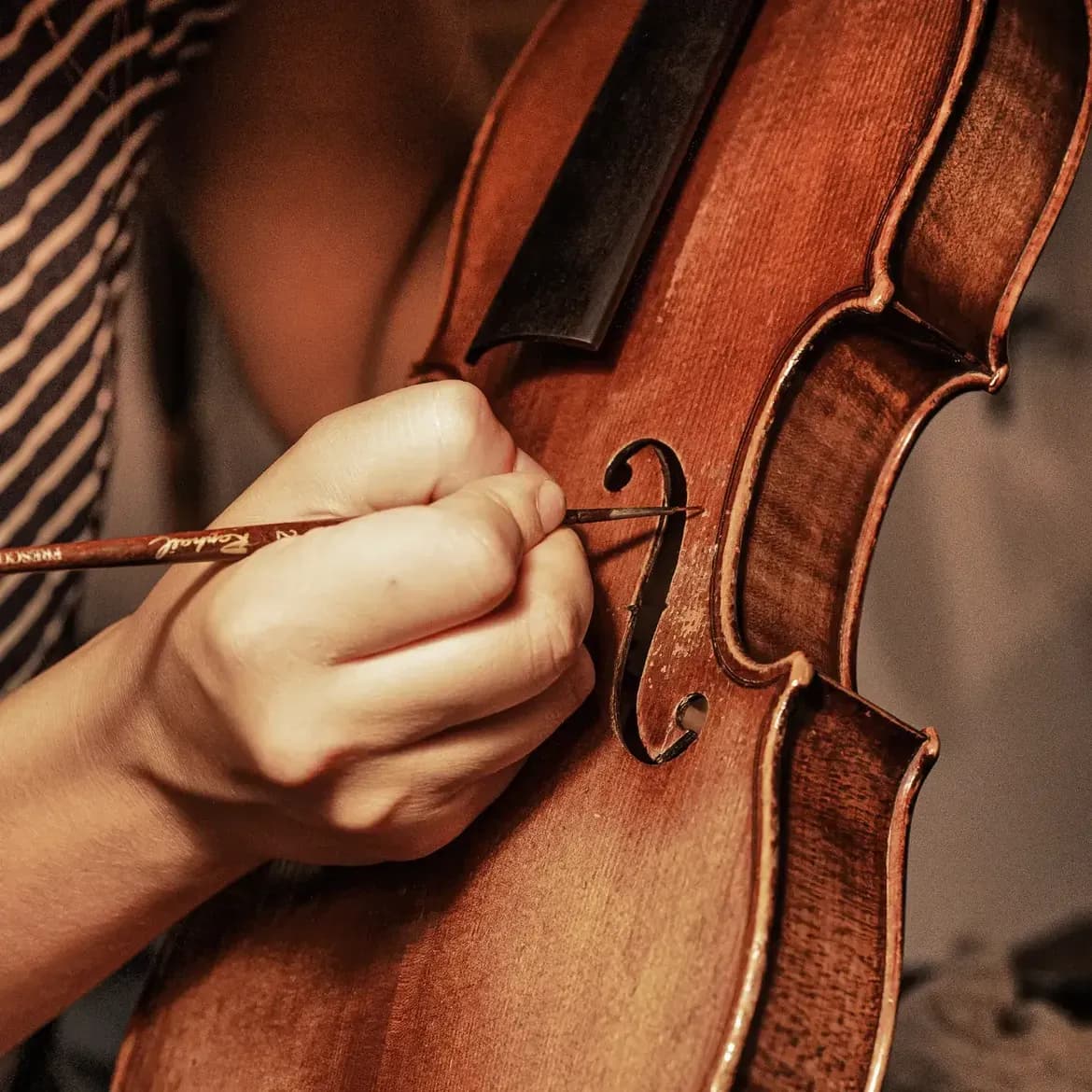 Gros plan sur un pinceau fin retouchant le vernis au bord d’une ouïe de violon