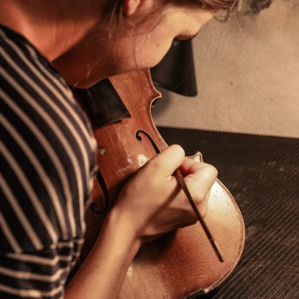Une luthière retouche au pinceau le vernis d’un violon tenu contre son épaule, près de l’ouïe