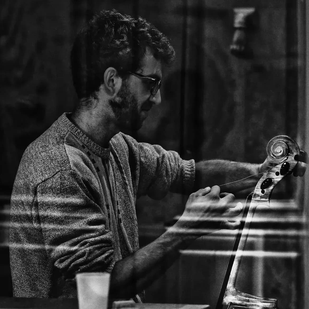 Un luthier tend une corde au chevillier d’un violoncelle, dans l’atelier