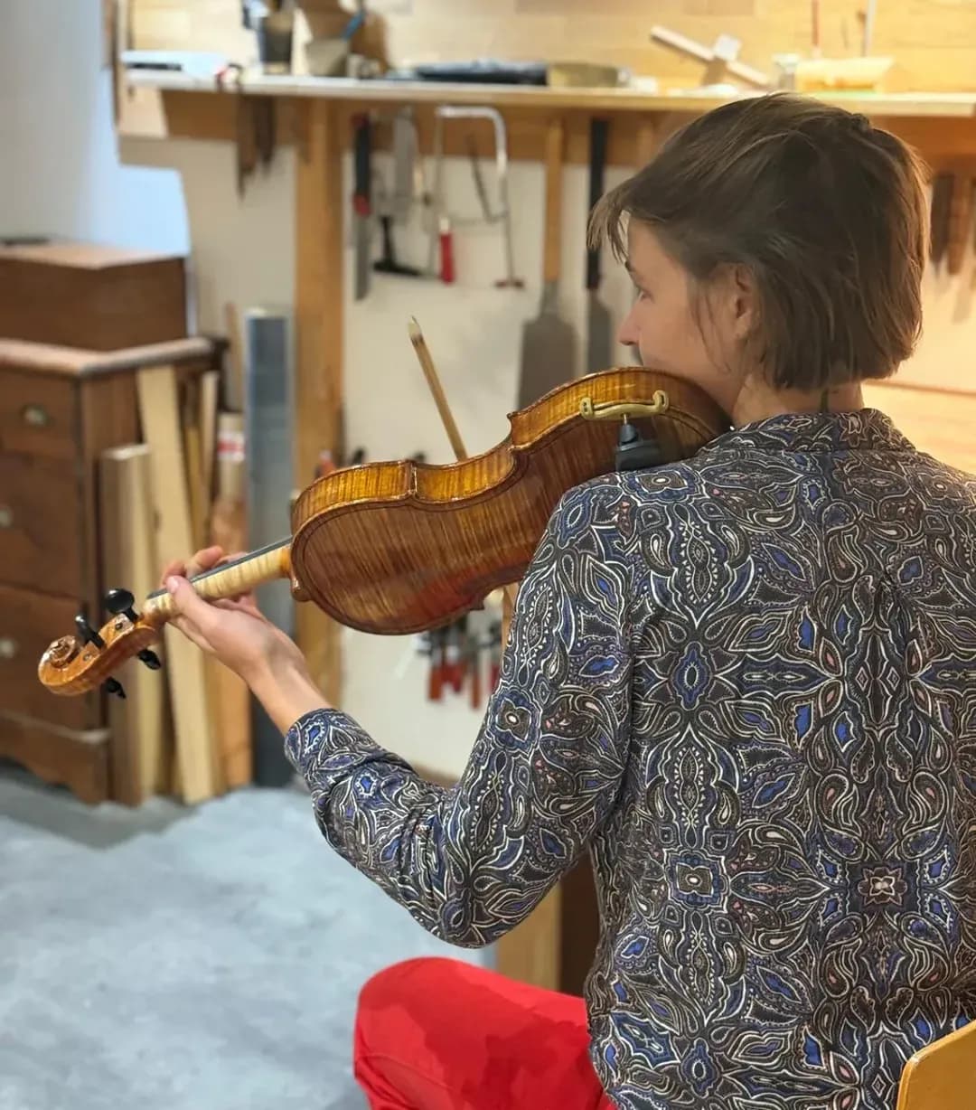 Une luthière tient un violon contre son épaule pour en vérifier le réglage, dans l’atelier