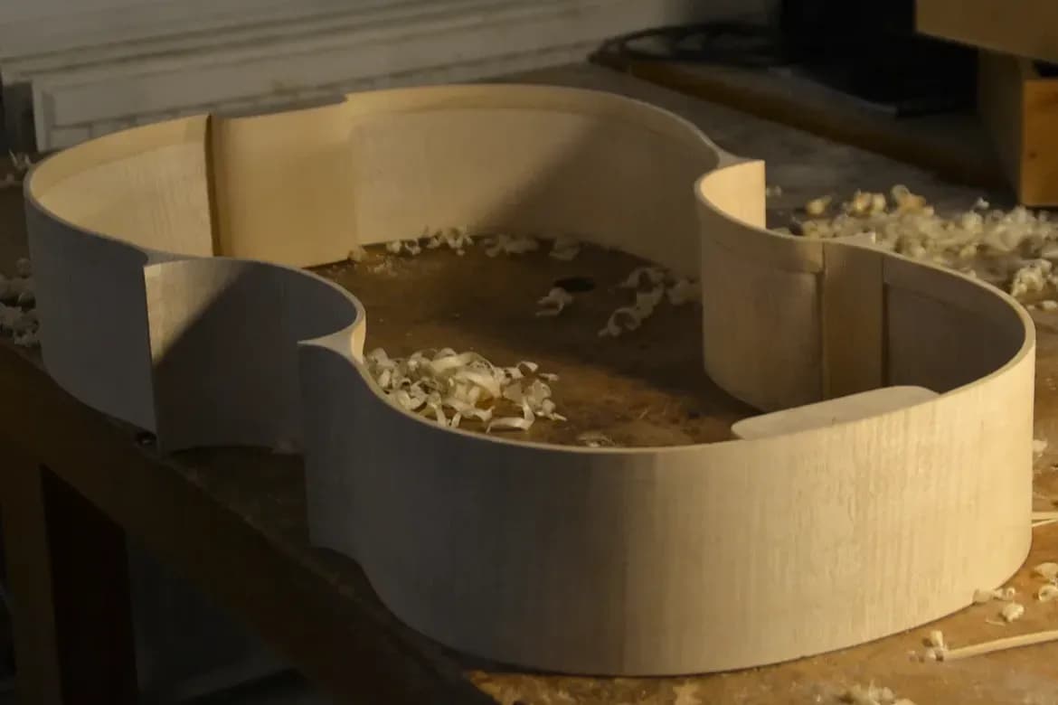 Couronne d’éclisses complète d’un violoncelle posée sur l’établi, copeaux de bois alentour
